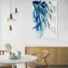 Tao te Ching Whispers - Original artwork of a blue green leaves hanging from above and gently blowing in the breeze. The hanging leaves contain reflections from the light above. There is Asian calligraphy on the right-hand side from the Tao te Ching regarding living a beneficial life. The painting conveys a sense of spirituality and elegance. The painting is shown hanging on a pale wall in a dining room.