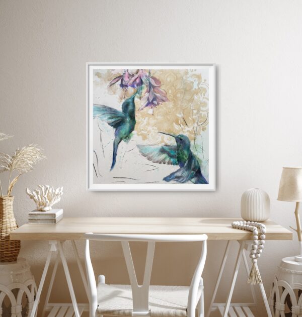 Hummingbird Jewels - original artwork of two jade hummingbirds flying up towards pink / purple fuchsia flowers with an ochre mandala pattern in the background hanging on a beige wall in front of a desk and chair.
