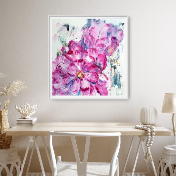 Luscious Pink - a mixed media artwork portrays the natural beauty of vibrant, luscious pink abstracted flowers surrounded by an abstract background containing beautiful blues, ochres, and uplifting writing. The painting is hanging on a pale wall with a desk and chair in front holding decorating items.