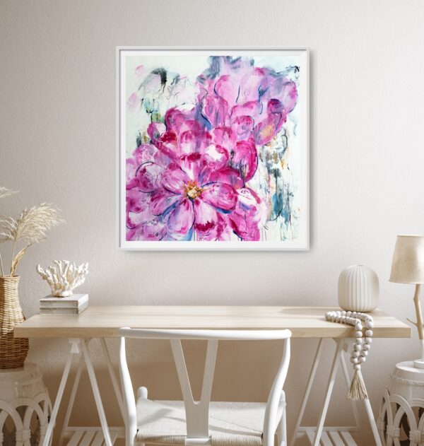 Luscious Pink - a mixed media artwork portrays the natural beauty of vibrant, luscious pink abstracted flowers surrounded by an abstract background containing beautiful blues, ochres, and uplifting writing. The painting is hanging on a pale wall with a desk and chair in front holding decorating items.