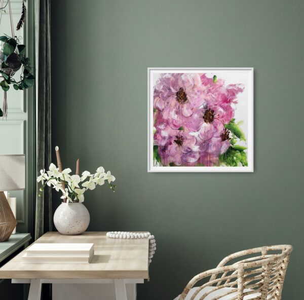 Opulent Pink - A mixed media painting portraying large, vibrant, and opulent pink flowers amongst green leaves in the background. The painting is hanging on a green wall with a pale desk and cane chair. Decorating items are on the desk.