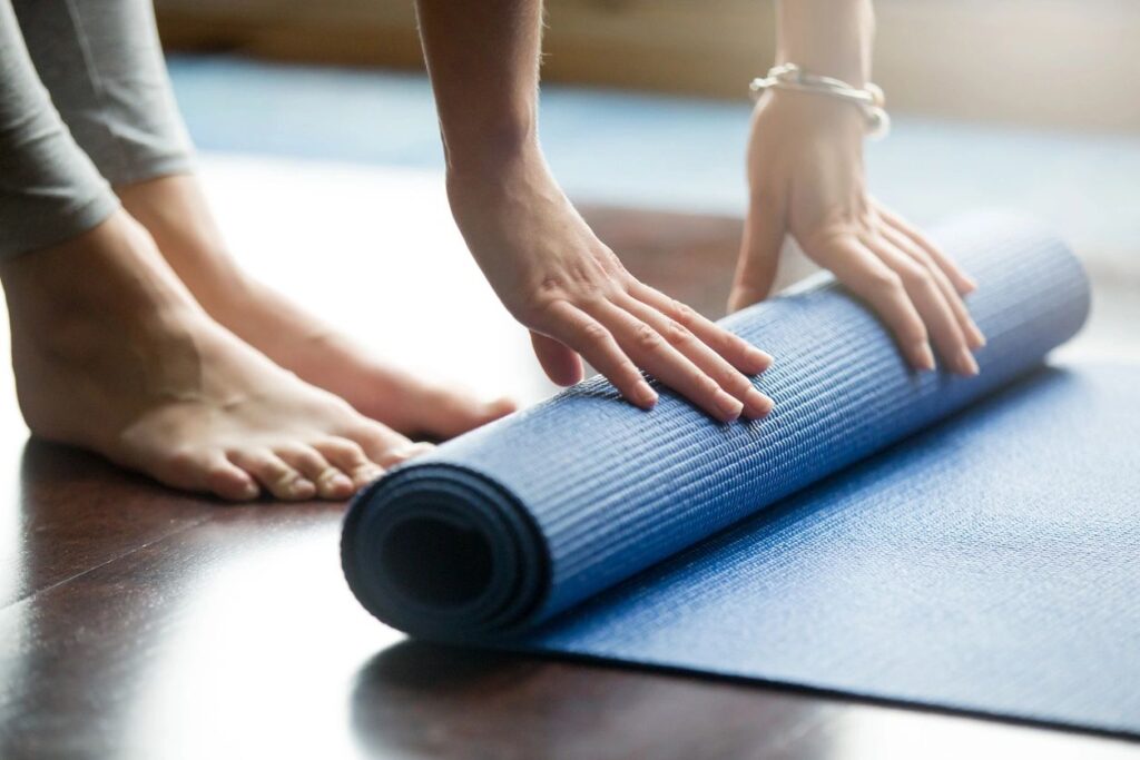 Photo of a yoga mat, hands and feet as the person rolls the mat up