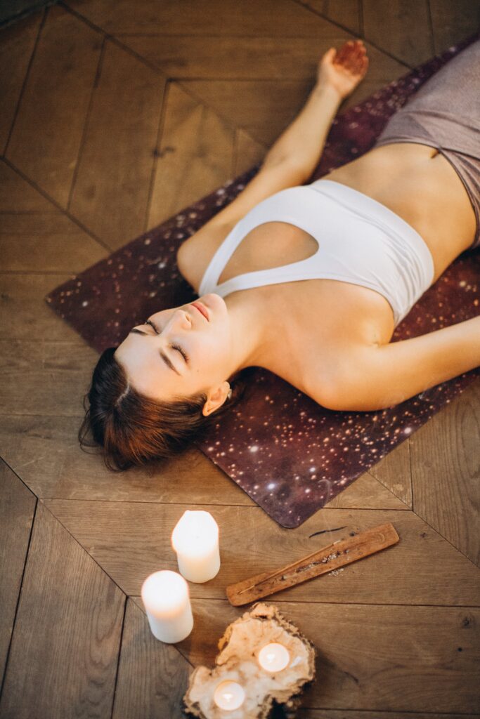 Woman lying on a yoga mat in relaxation with incense and candles beside her.
