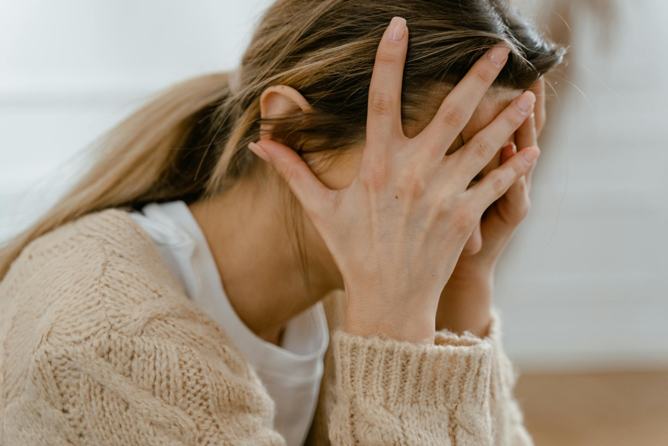 Woman sitting indoors with face covered by hands, expressing stress and frustration.